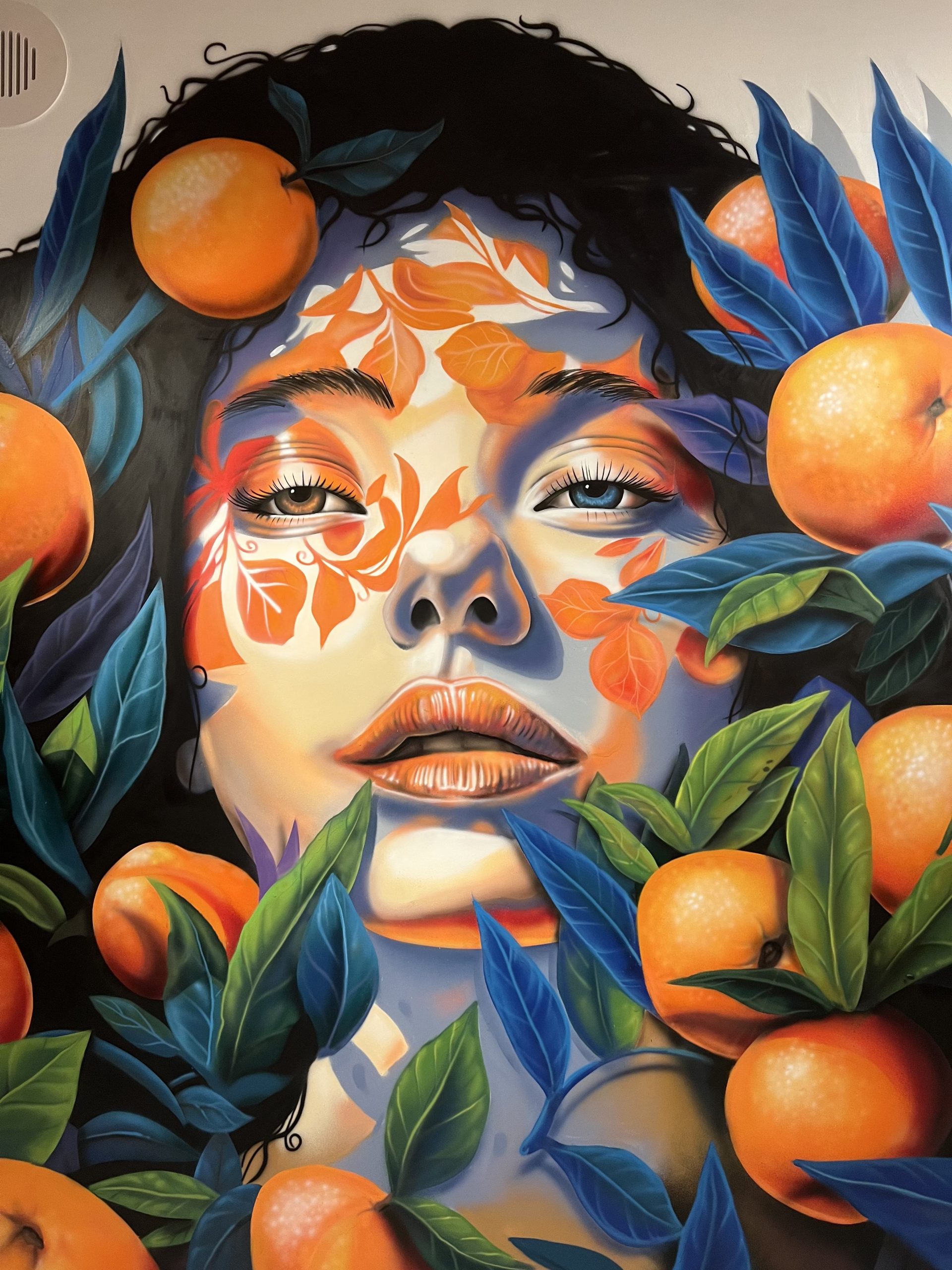 Close-up detail of photorealistic airbrushed portrait mural with orange fruit and blue botanical foliage