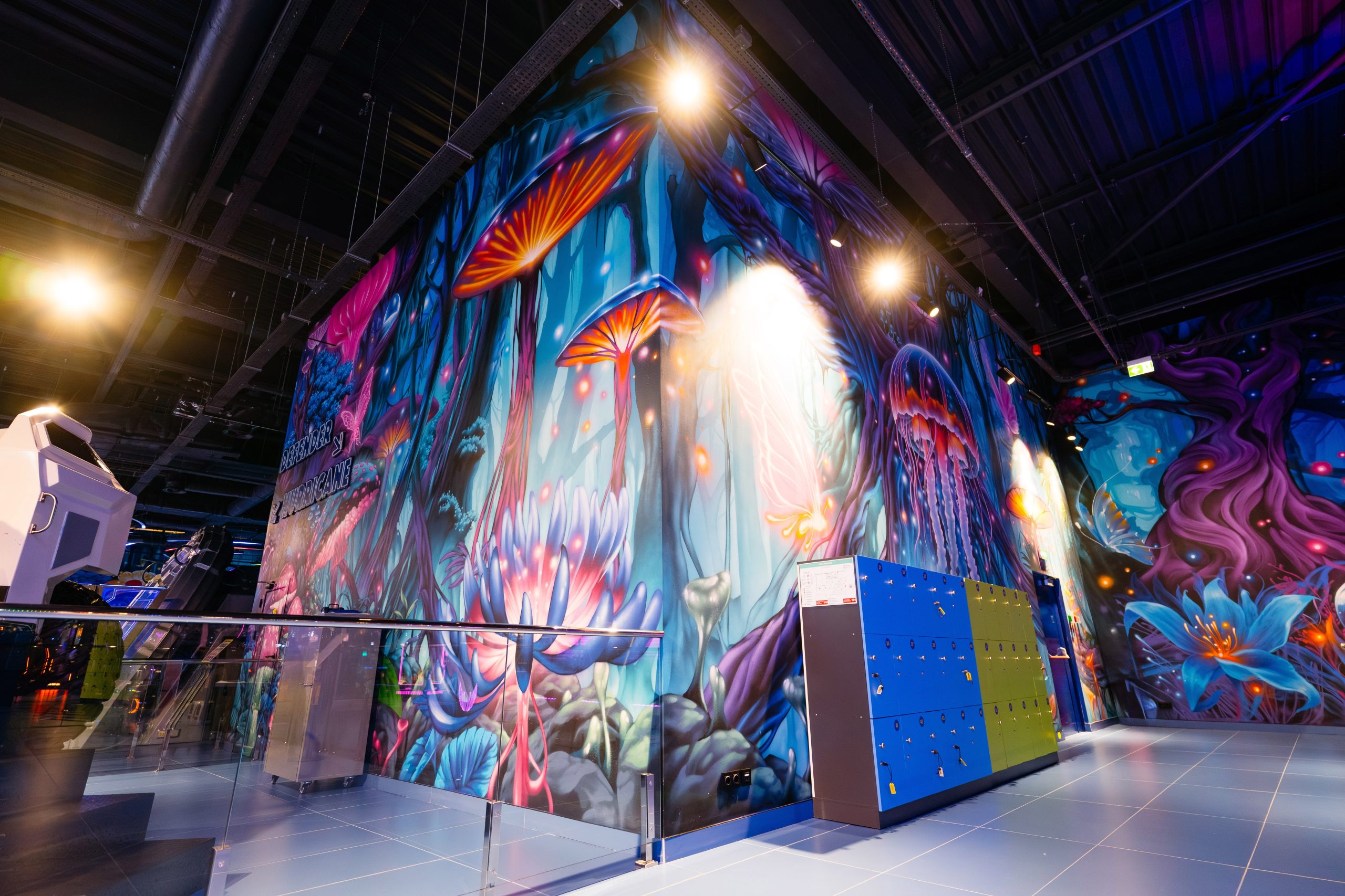 Arcade gaming area with large-scale fantasy wall mural featuring luminescent mushrooms and surreal vegetation creating immersive entertainment environment