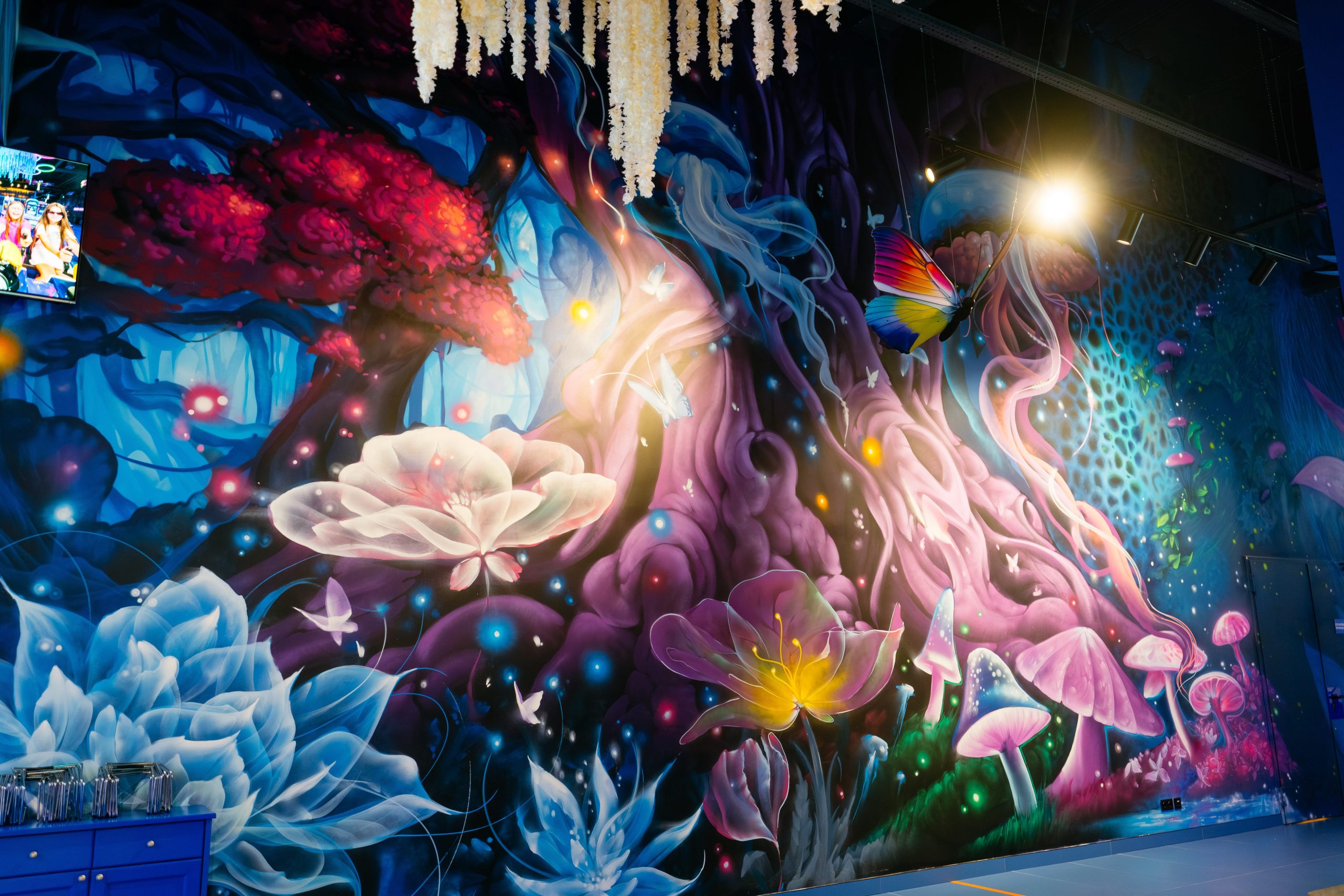 Detailed close-up of hand-painted bioluminescent flowers and butterflies in neo-surrealist interior mural showing multi-layered luminescent pigment technique