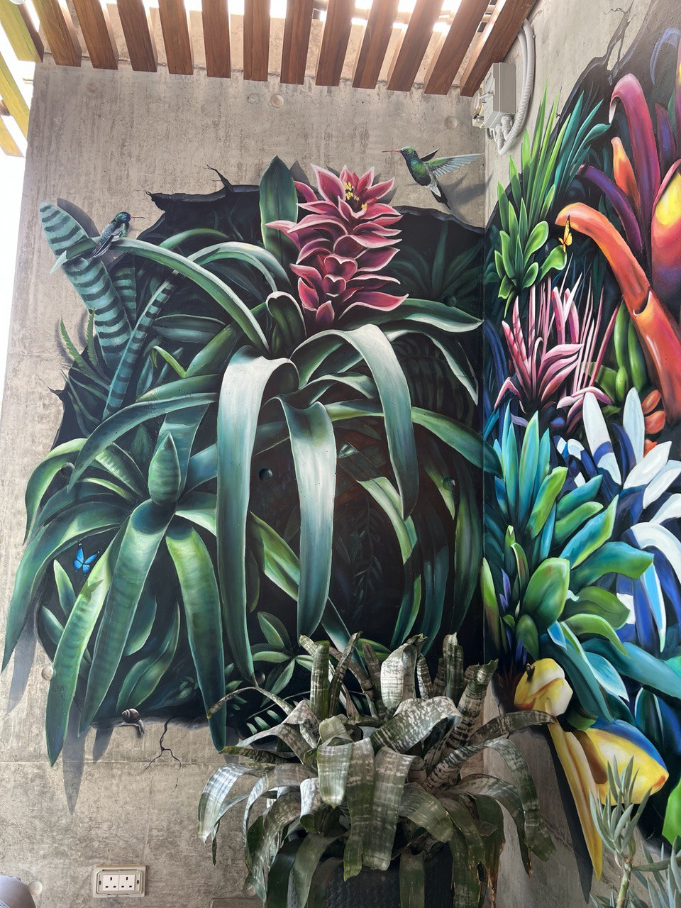 Close-up detail of hyperrealistic tropical mural showing pink bromeliad flowers and green foliage on concrete wall