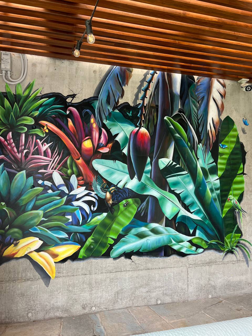 Close-up of hyperrealistic tropical foliage mural showing airbrushed banana leaves and exotic flowers