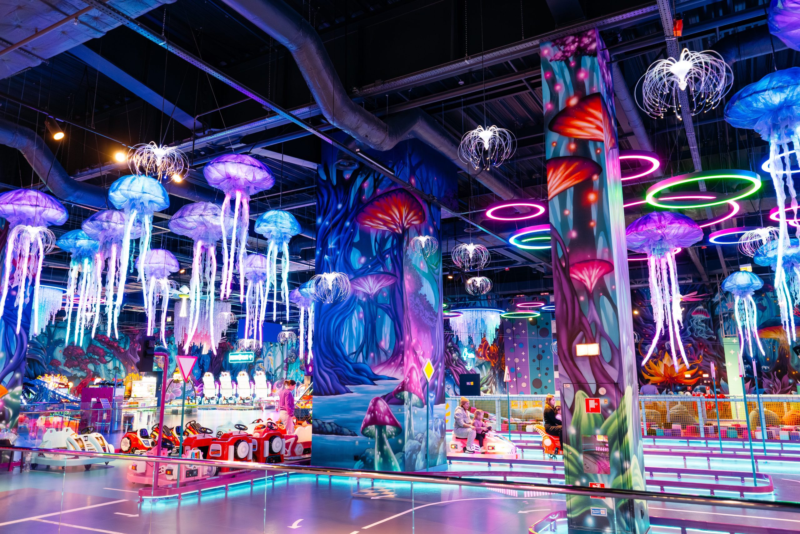 Immersive children's entertainment area with fantasy wall and ceiling murals featuring hanging jellyfish sculptures and bioluminescent underwater theme