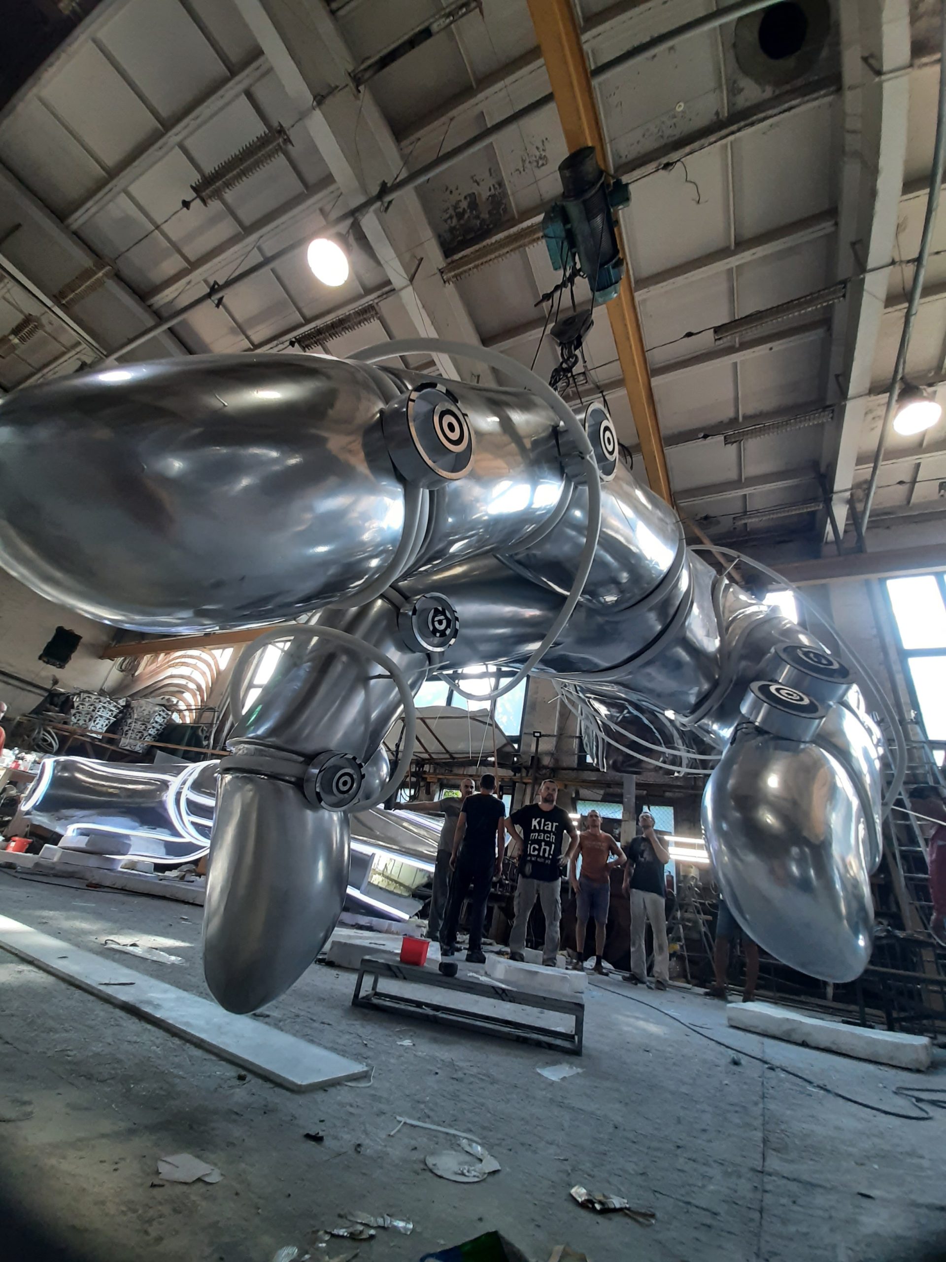 Large-scale metal hand sculpture showing size with fabrication team in industrial workshop