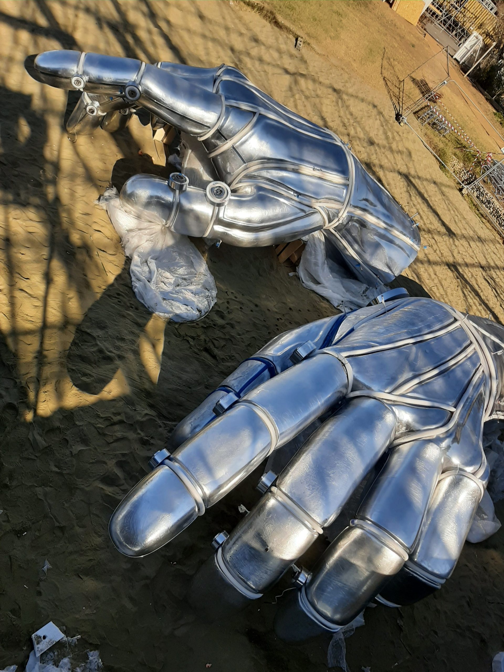 Aerial view of metal hand sculpture components laid out on ground before assembly