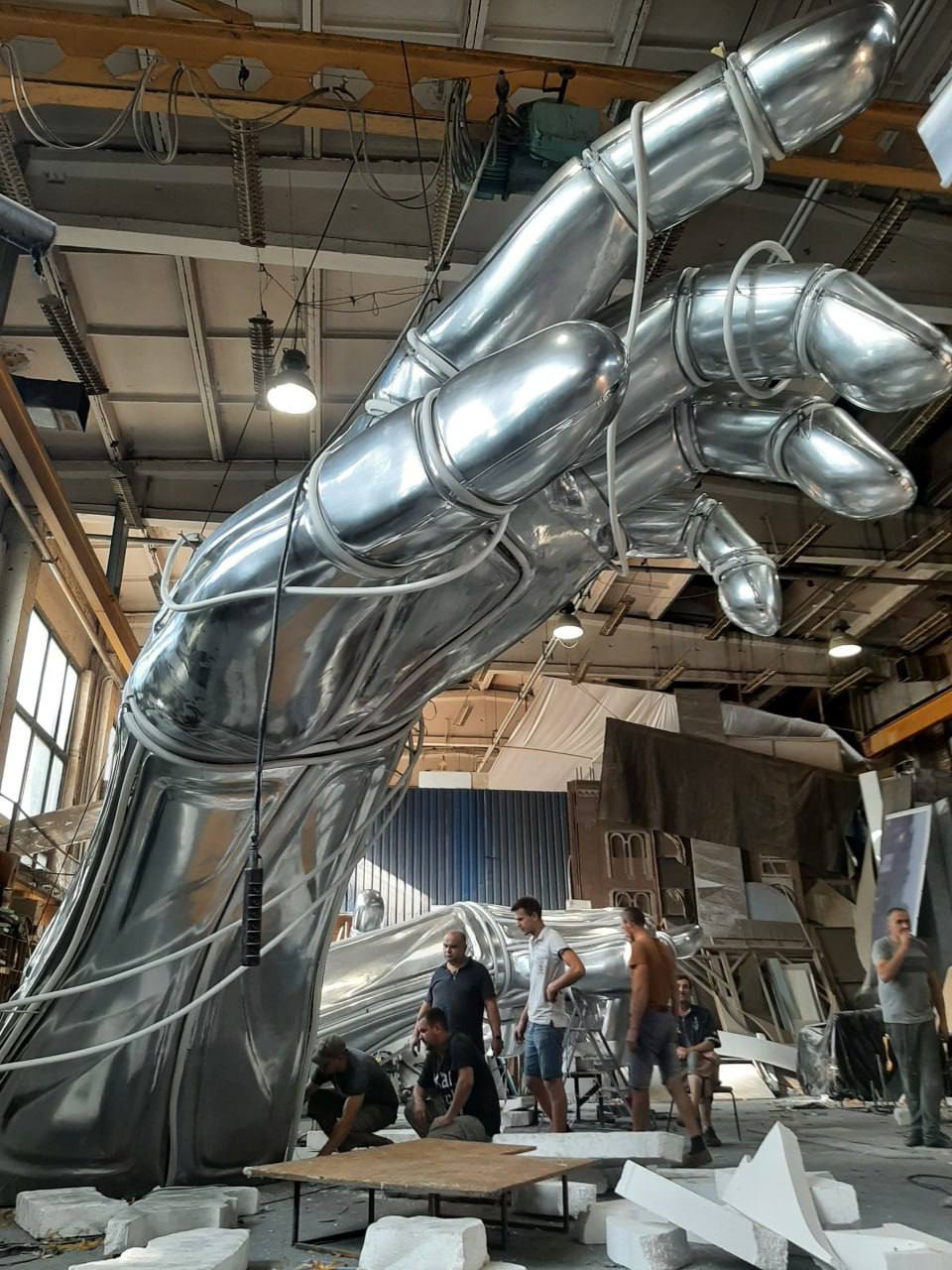 Metal hand sculpture being lifted by crane during outdoor installation against blue sky