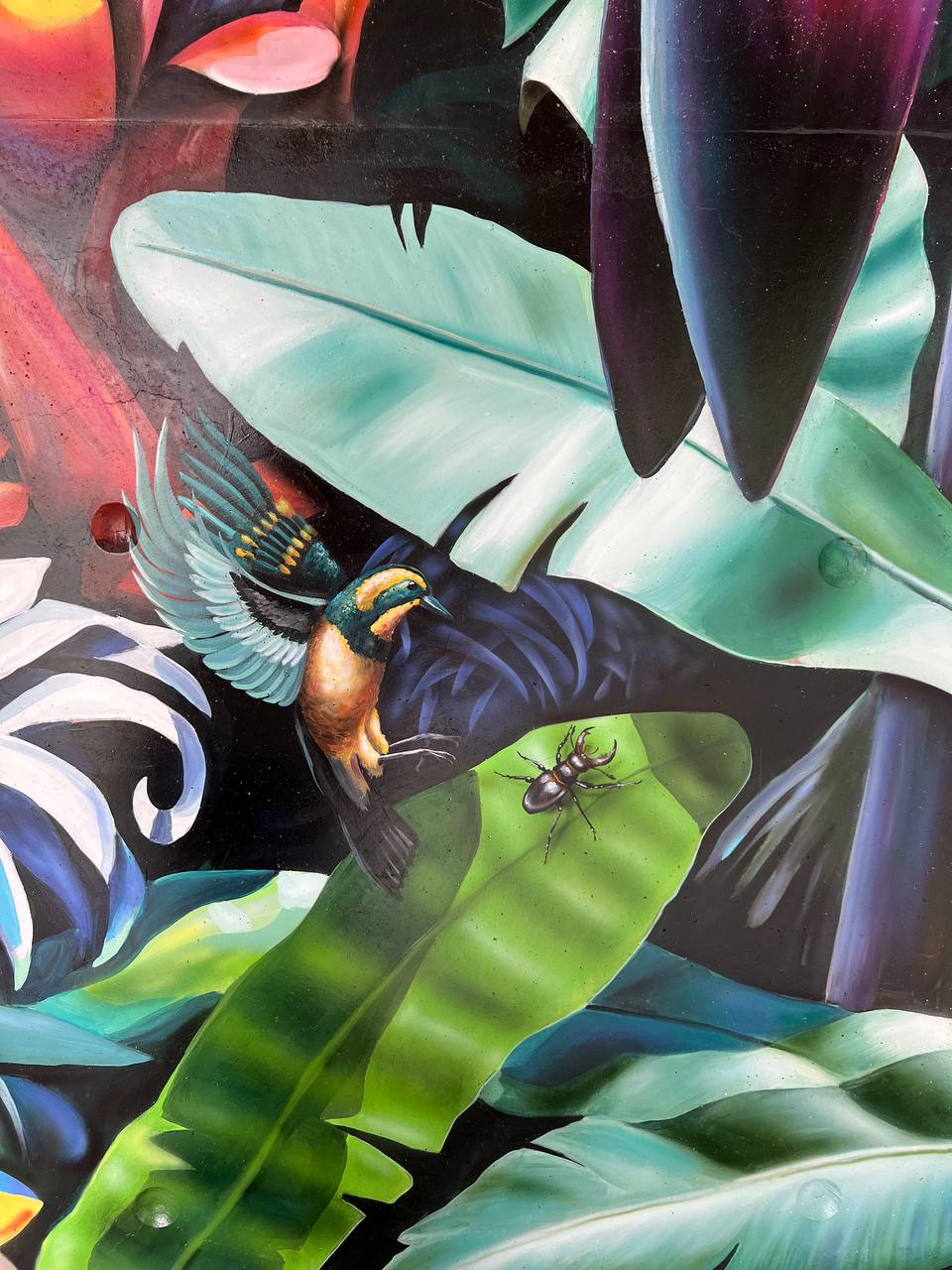 Extreme close-up of mural detail showing kingfisher bird with iridescent feathers on banana leaf