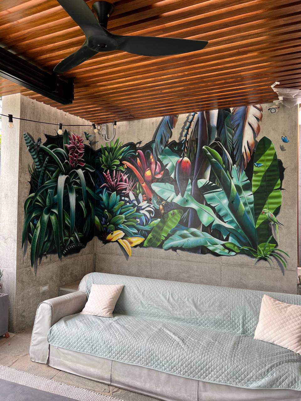 Covered outdoor terrace with large botanical wall mural featuring 3D illusion tropical garden design under wooden ceiling