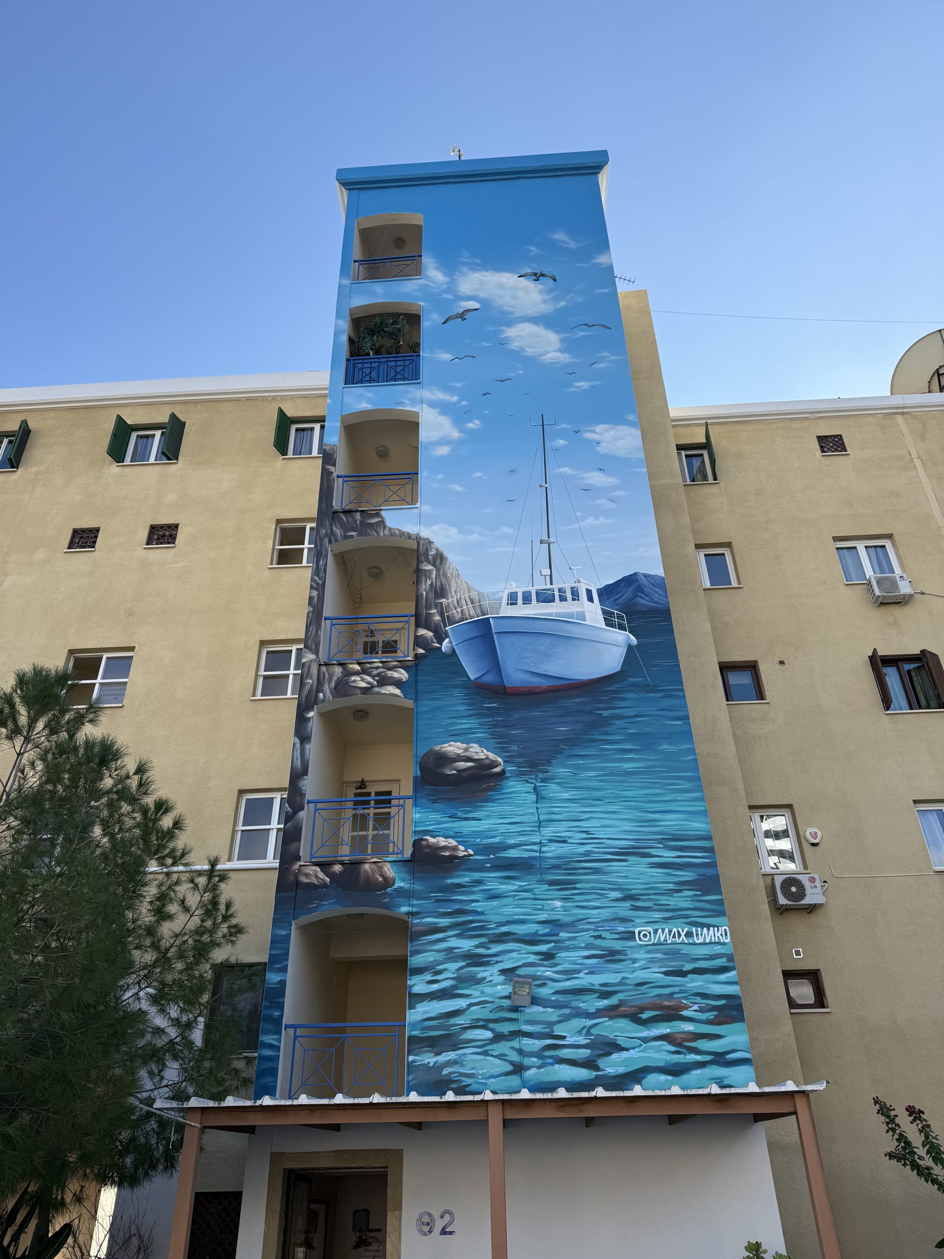 Maritime-themed building mural featuring boat on calm water in bright daylight