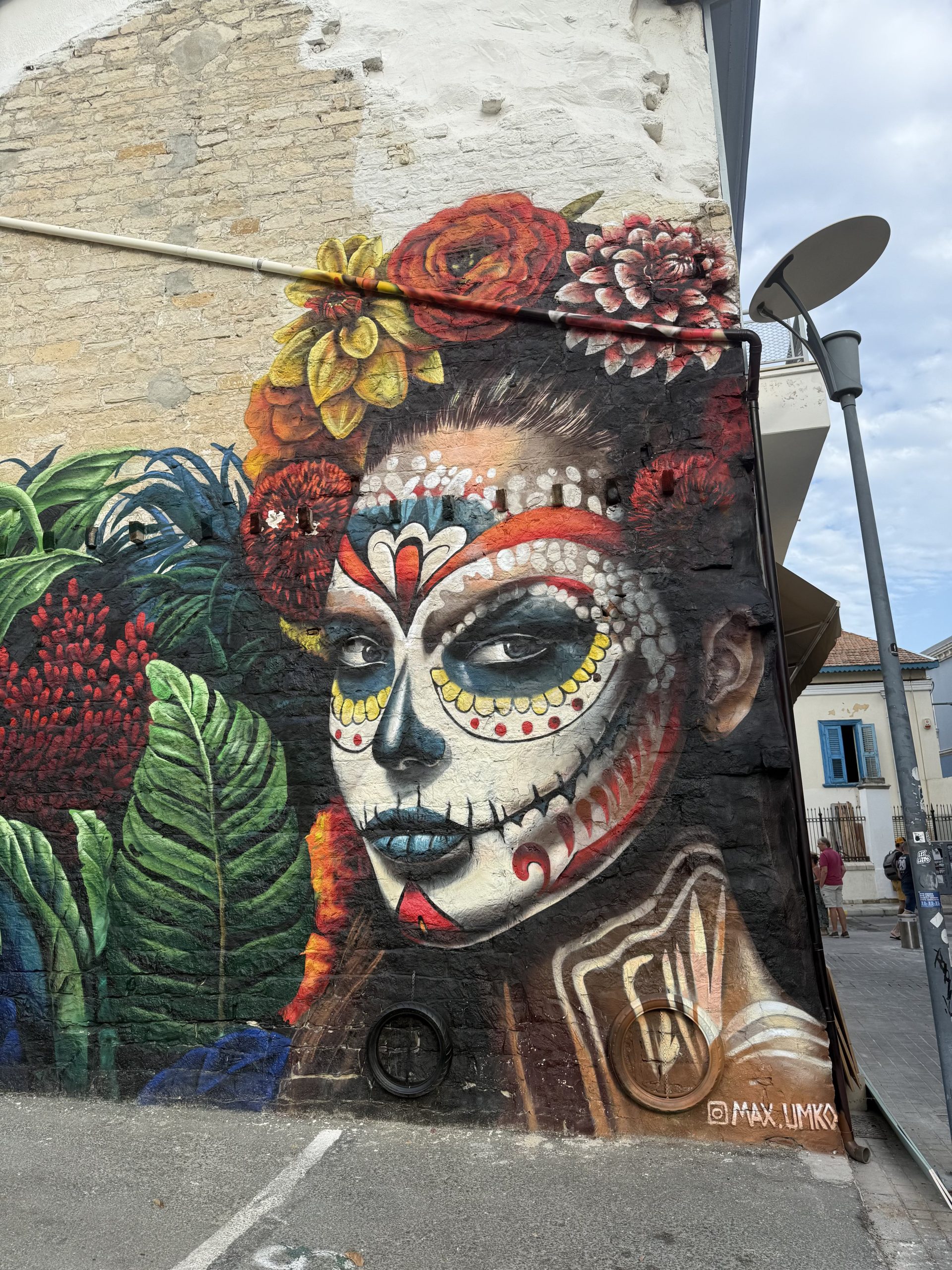 Large-scale La Calavera Catrina mural on restaurant exterior wall with tropical foliage and Day of the Dead imagery