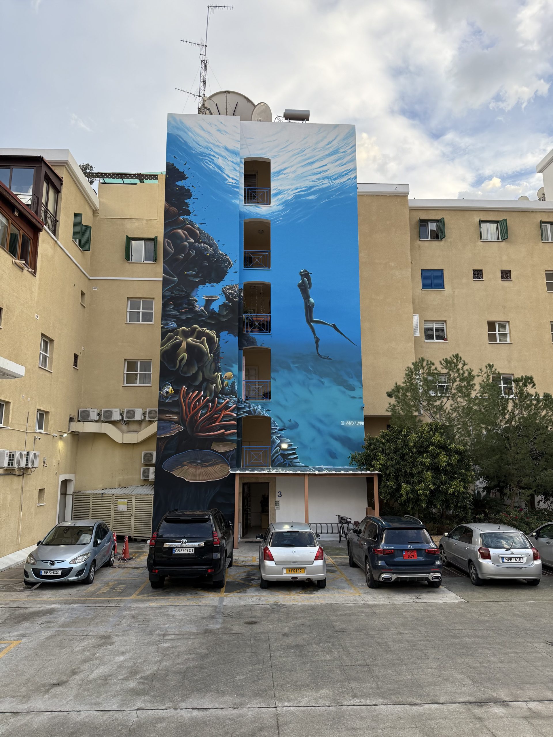 View of large underwater-themed building mural from parking area showing coral and diver